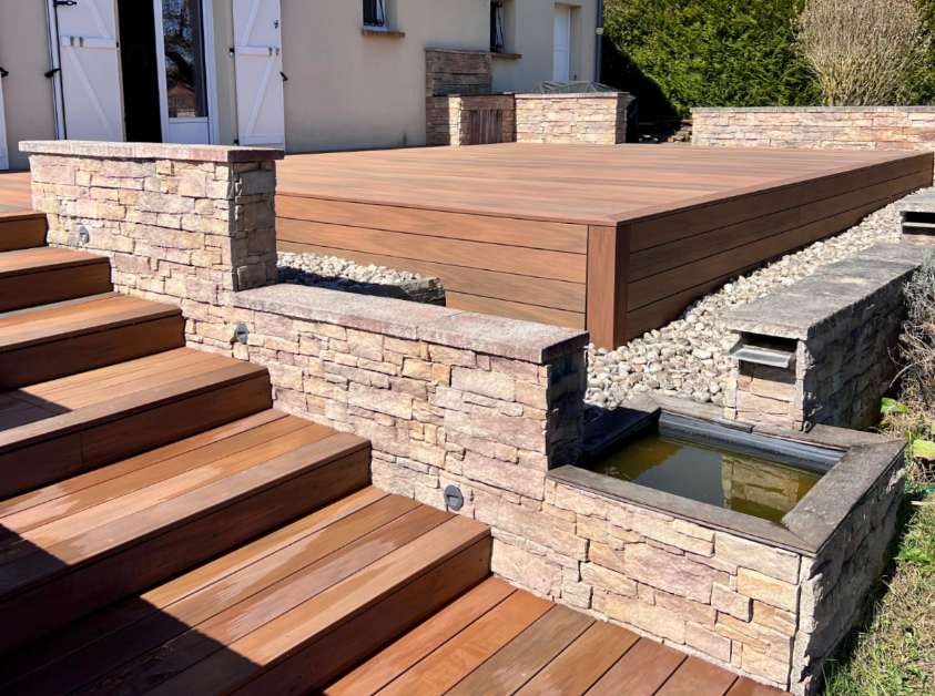 Terrasse en bois composite avec escalier intégré et murets en pierre naturelle réalisée par Agave Paysage