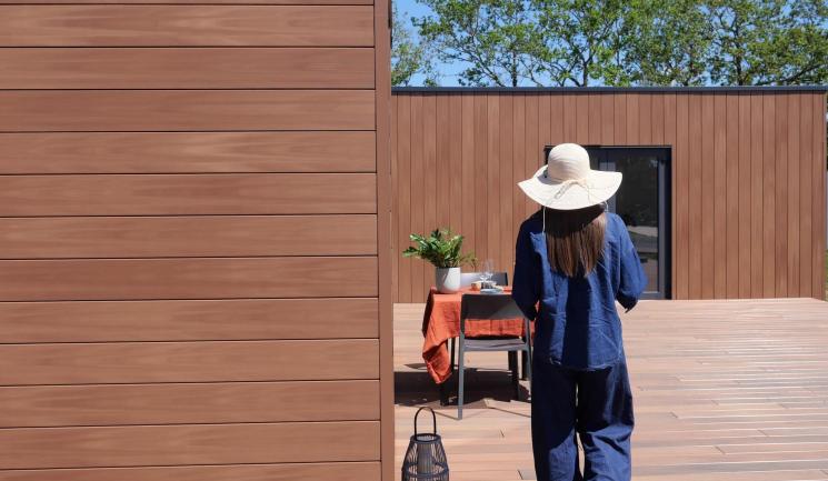 Jeune femme au chapeau marche vers une table et Bardage Atmosphère 175 Brun Soleil Silvadec 